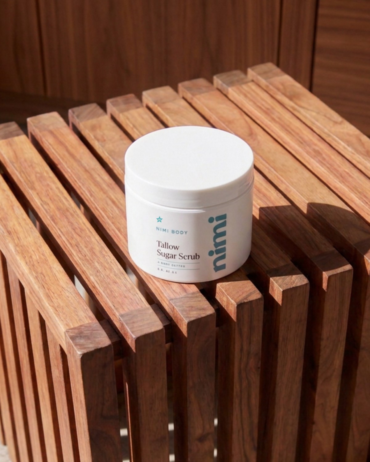 Nimi Tallow Sugar Scrub on a teak shower stool in morning light